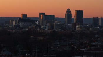 A silhouetted skyline of Louisville, Kentucky, at dusk with buildings against a colorful sunset background.