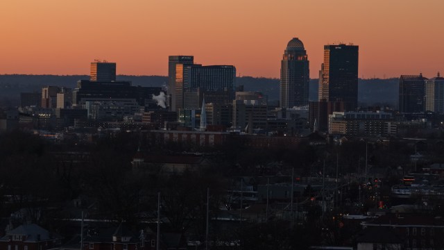 A silhouetted skyline of Louisville, Kentucky, at dusk with buildings against a colorful sunset background.