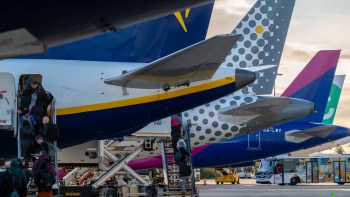 Passengers boarding a plane with various airline tails visible in the background at an airport terminal.