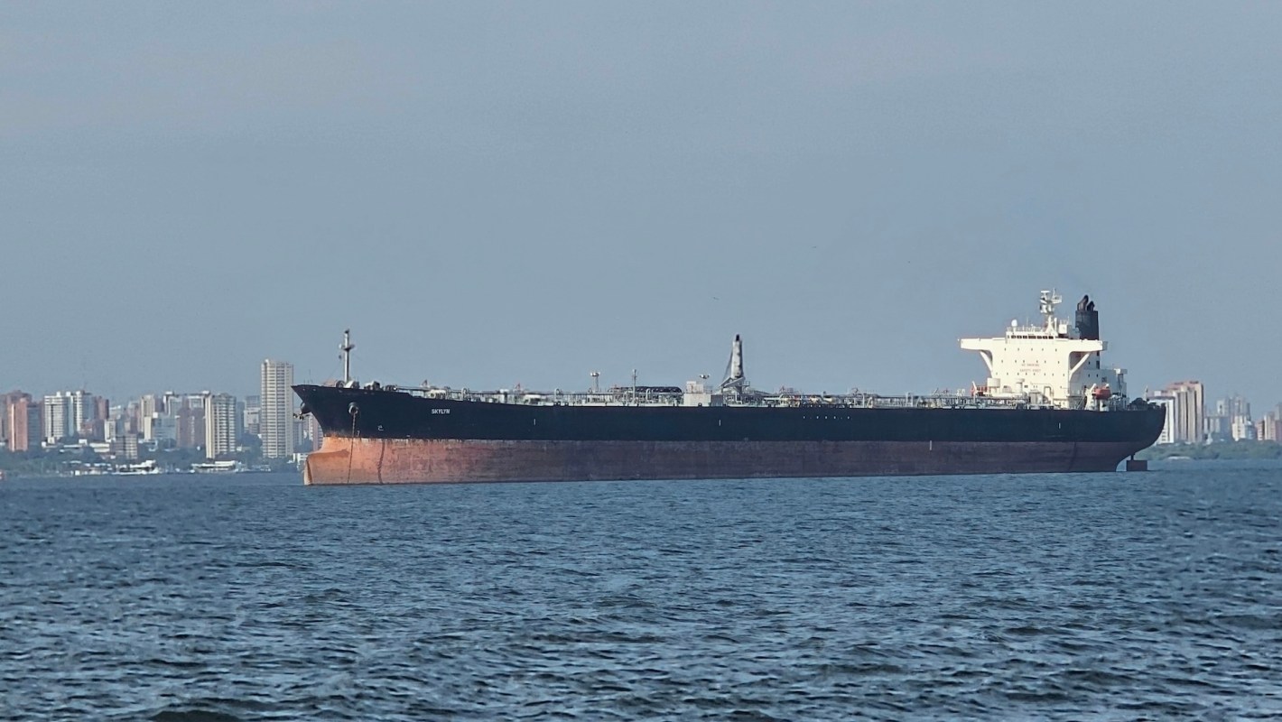 A large oil tanker anchored in calm waters with a city skyline in the background.