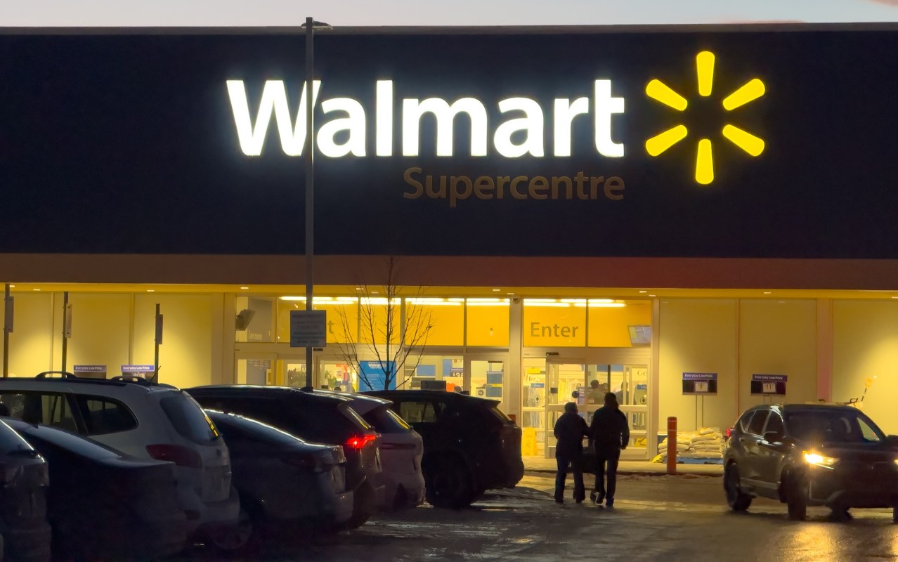 A Walmart Supercentre entrance lit up at night with shoppers walking toward the door.