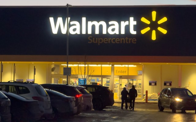 A Walmart Supercentre entrance lit up at night with shoppers walking toward the door.