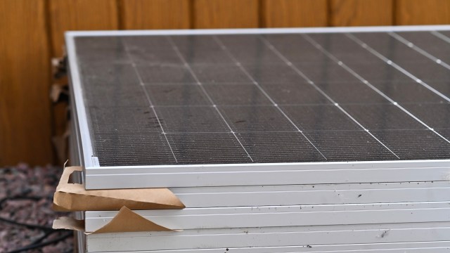A close-up of a stacked solar panel with a wooden background and some dirt on the surface.