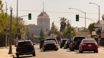A busy street scene with cars and green traffic lights, featuring a tall building in the background.
