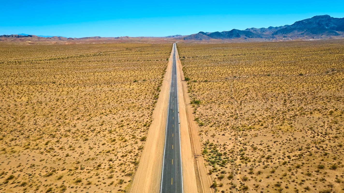 A long, straight road stretches through desert landscape under a clear sky.