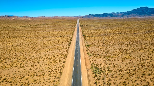 A long, straight road stretches through desert landscape under a clear sky.