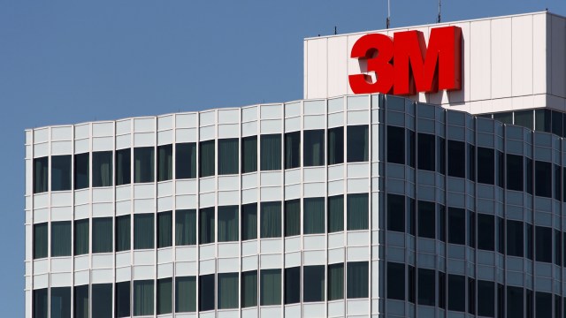 The top of a glass office building featuring the large red "3M" logo against a clear blue sky.
