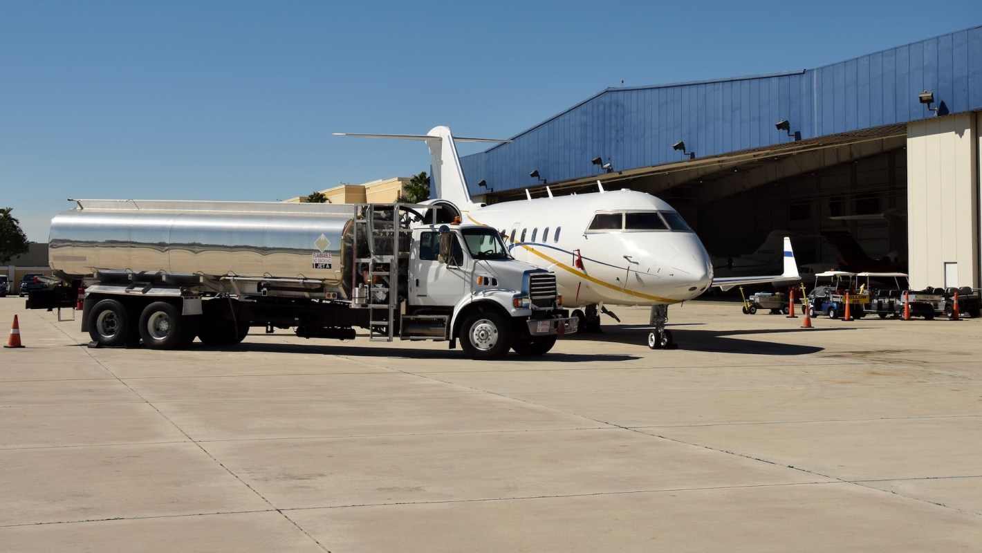 A fuel truck is parked next to a private jet at an airport hangar under a clear blue sky.