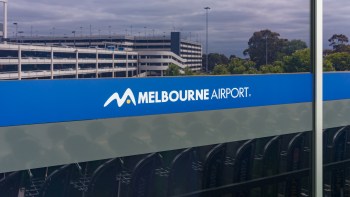 A sign displaying the logo and name of Melbourne Airport beside a parking structure.
