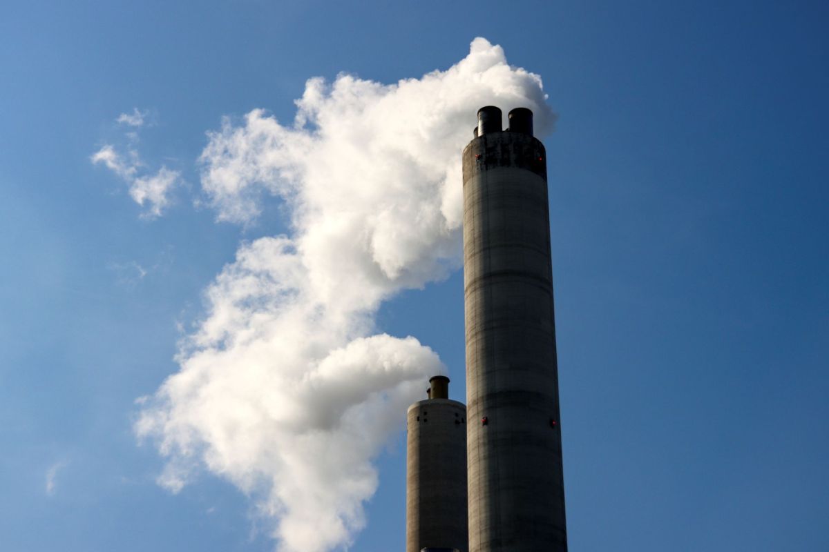 Two tall smokestacks emitting white smoke against a clear blue sky.