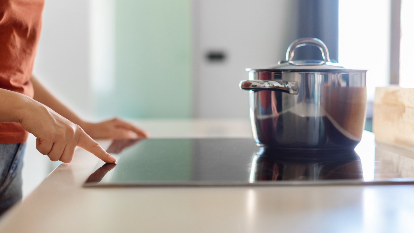 A person turns on a sleek induction cooktop with a pot on the back burner.