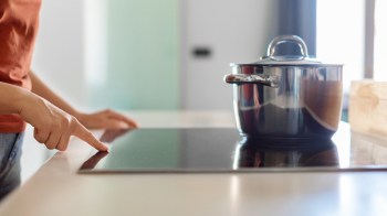 A person turns on a sleek induction cooktop with a pot on the back burner.