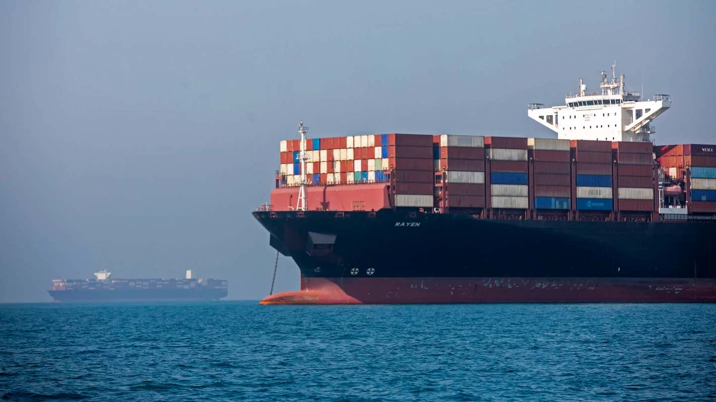 Two large cargo ships are anchored in calm waters under a hazy sky.