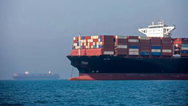 Two large cargo ships are anchored in calm waters under a hazy sky.