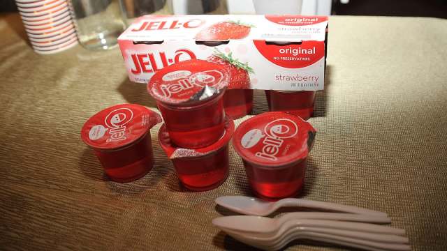 A stack of strawberry Jell-O cups with a box and plastic spoons on a textured surface.