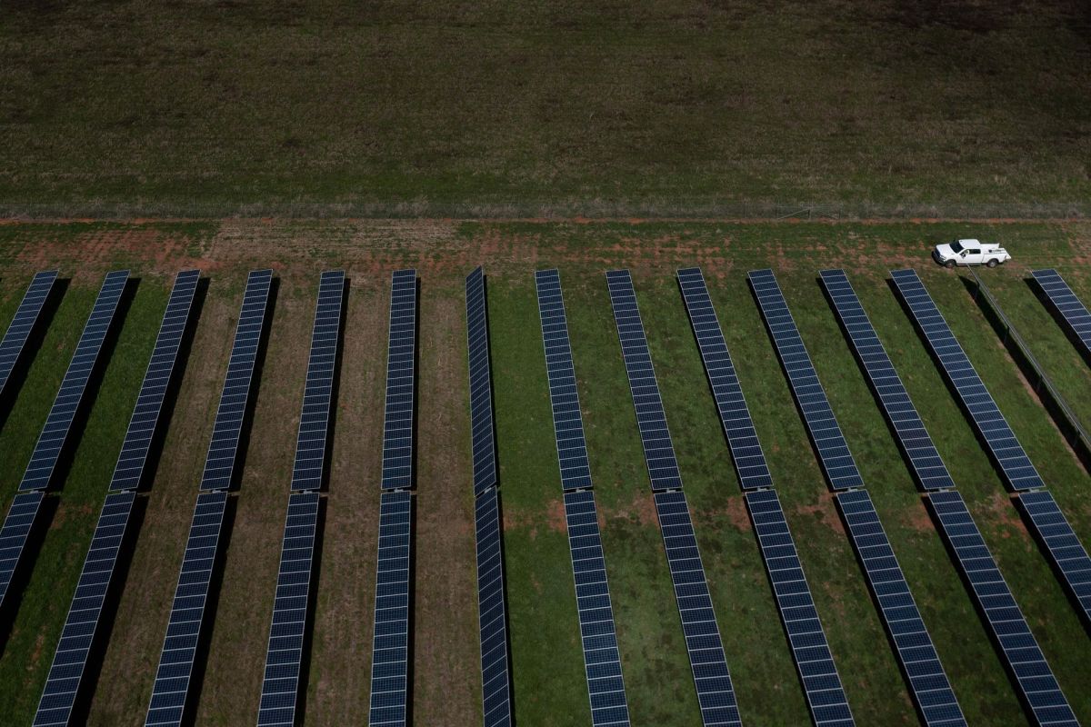 Aerial view of a solar farm with rows of solar panels and a white vehicle parked nearby.