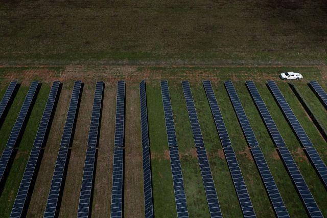Aerial view of a solar farm with rows of solar panels and a white vehicle parked nearby.
