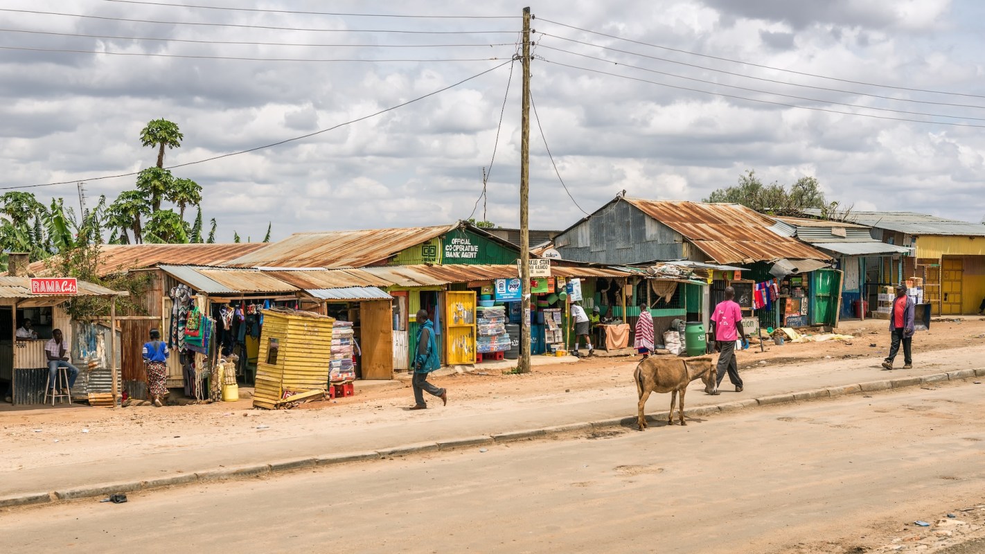 A vibrant street scene with small shops, people walking, and a cow near dirt roads under a cloudy sky.