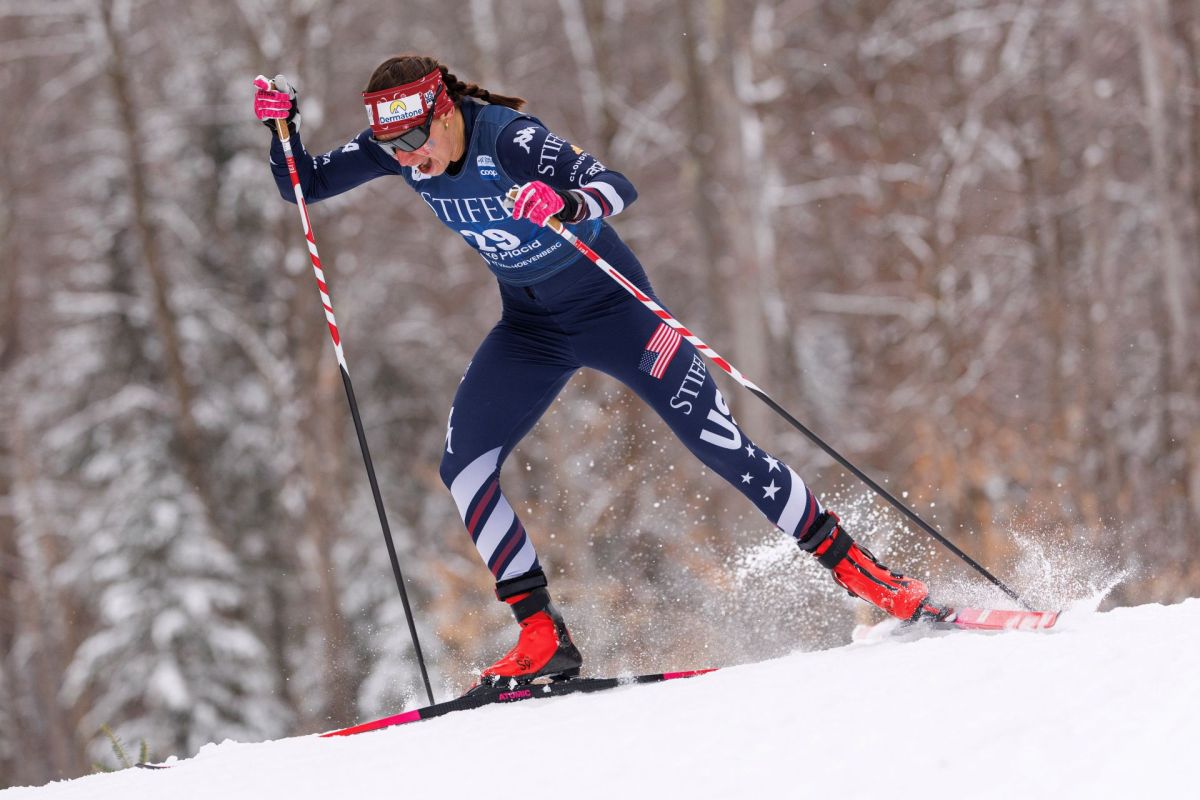 A competitive skier in a blue racing suit gracefully strides through the snowy landscape, creating a spray of snow.
