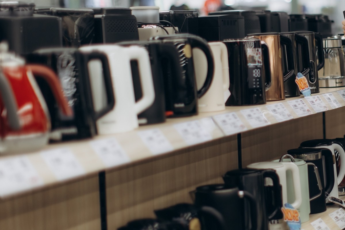 A shelf displaying various electric kettles in different colors with price tags underneath.