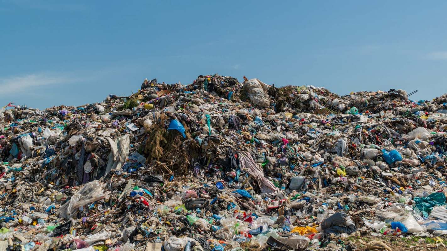 A large landfill with various types of trash and debris under a clear blue sky.
