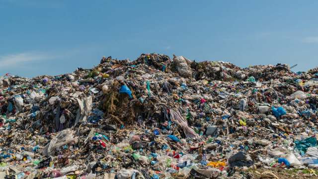 A large landfill with various types of trash and debris under a clear blue sky.