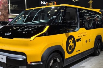 A yellow and black Kia taxi designed for accessibility, featuring a wheelchair symbol and NYC markings.