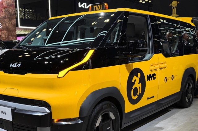 A yellow and black Kia taxi designed for accessibility, featuring a wheelchair symbol and NYC markings.