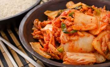 A bowl of kimchi with vibrant red chili and green onions, served alongside a bowl of white rice.