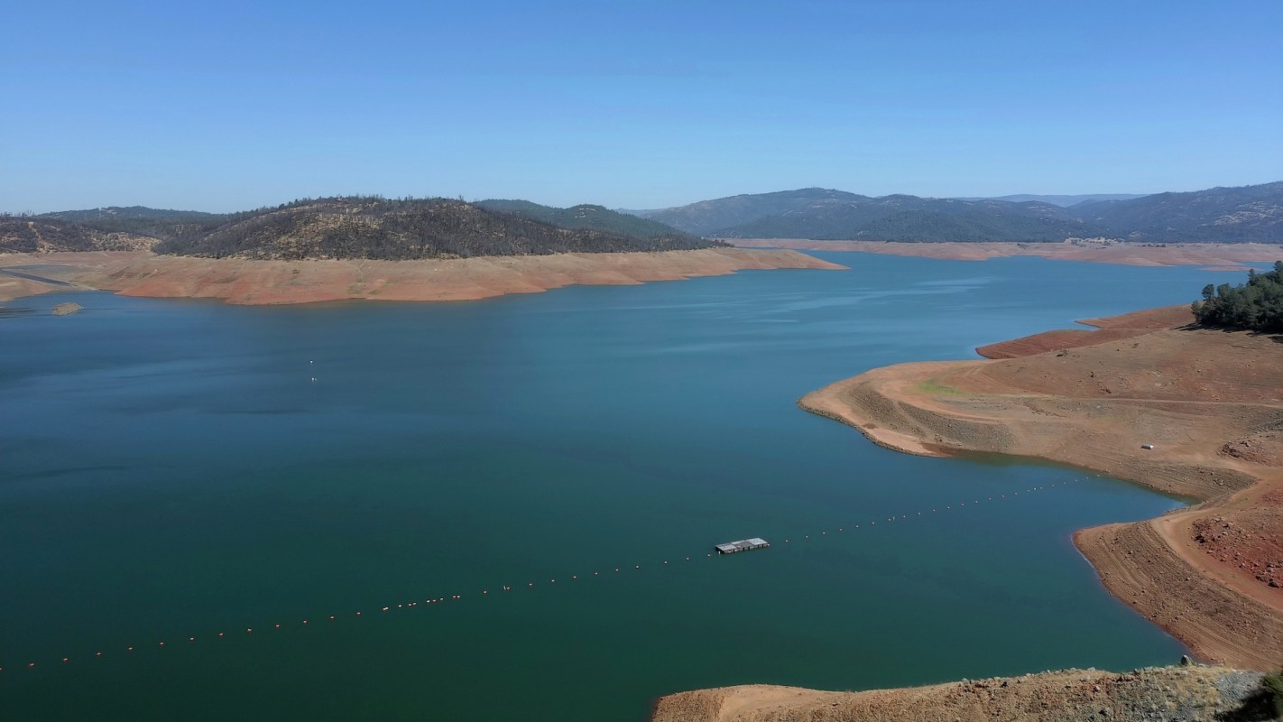 A tranquil lake surrounded by rocky shores and distant hills under a clear blue sky.