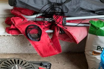 A close-up of a torn red fabric, a mesh pocket, and metal frame pieces resting on a garage floor with bags nearby.