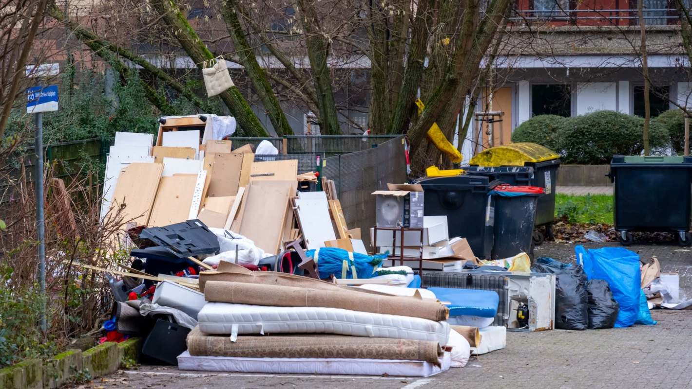 A pile of discarded furniture and trash near a recycling bin in an urban area.