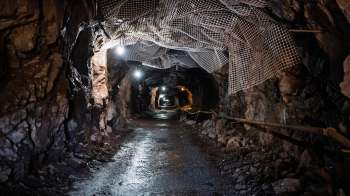 A dimly lit underground mine tunnel with rocky walls and support netting above.