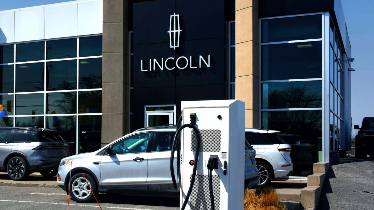 An electric vehicle charging station in front of a Lincoln dealership with several cars parked outside.
