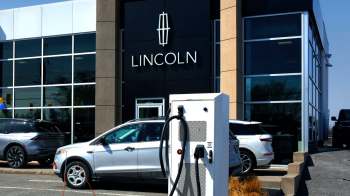 An electric vehicle charging station in front of a Lincoln dealership with several cars parked outside.