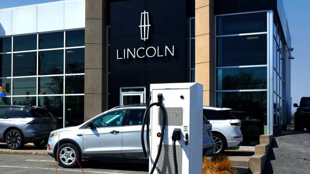 An electric vehicle charging station in front of a Lincoln dealership with several cars parked outside.