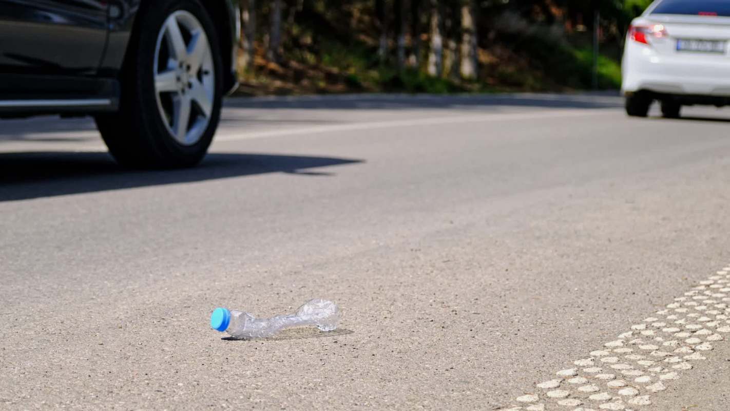 A plastic water bottle lies on a road next to passing cars.