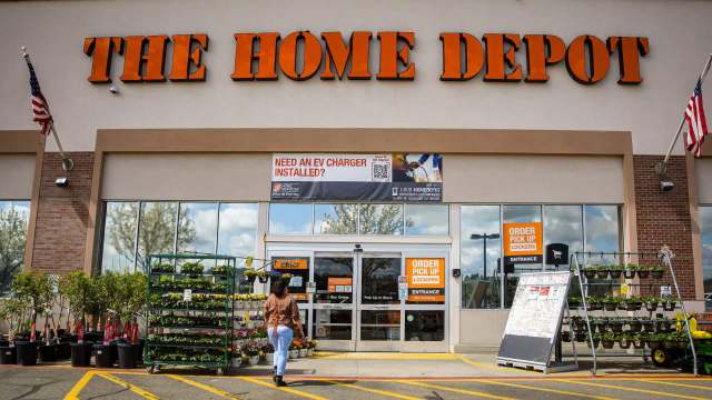 A customer approaches The Home Depot entrance with outdoor plants displayed nearby.