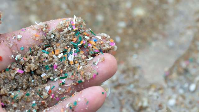 A hand holds a mixture of sand and colorful plastic debris on a blurred sandy background.