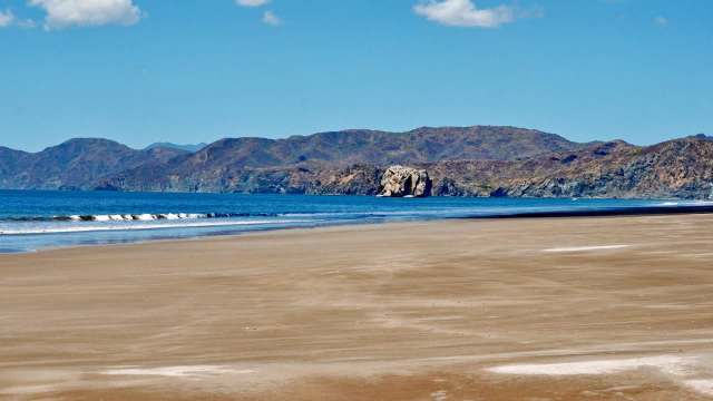 A serene beach scene with gentle waves and mountains in the background under a clear blue sky.