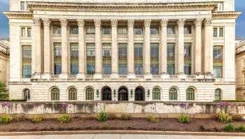 The United States Department of Agriculture building features classical architecture with tall columns and landscaped flower beds.