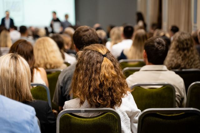 A crowd of people seated in a conference room, focusing on a presentation at the front.