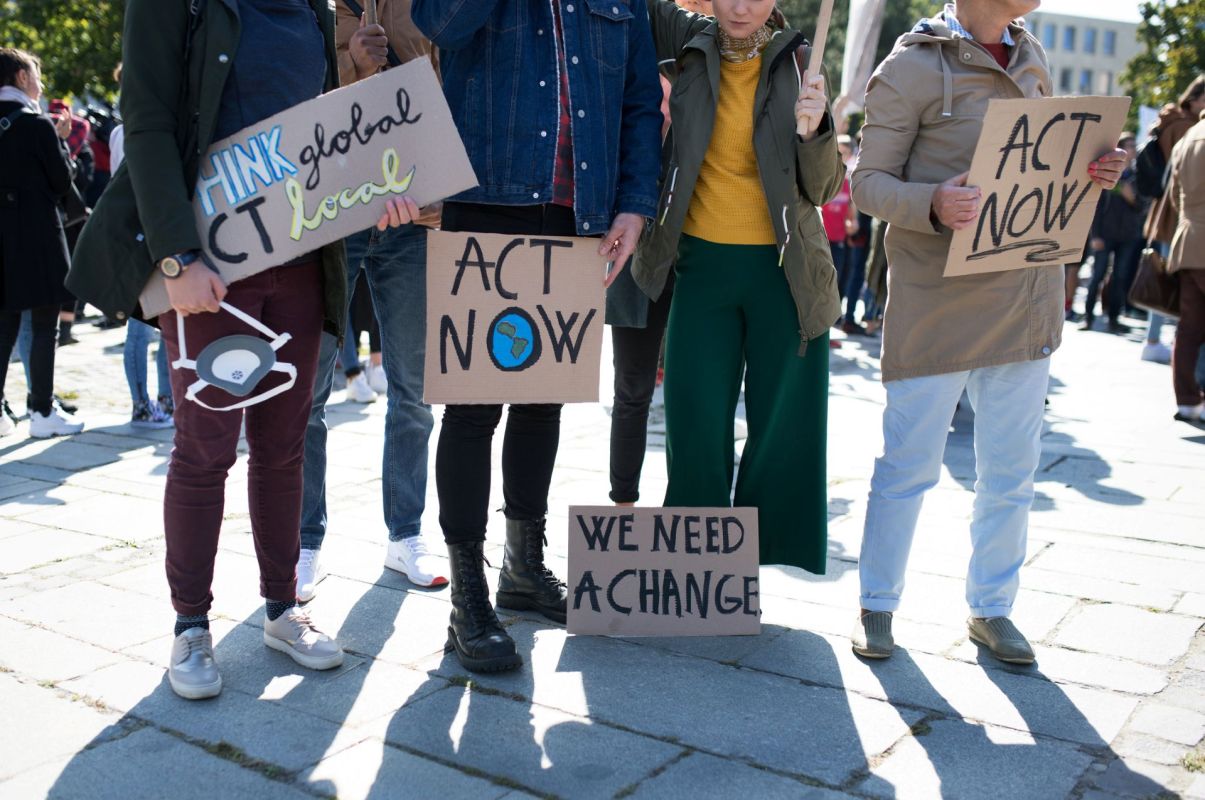 A group of protesters holding signs that read "act now," "we need change," and "think global act local."
