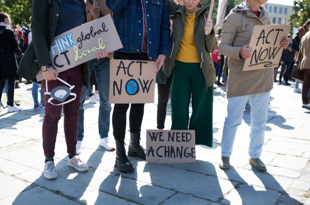 A group of protesters holding signs that read "act now," "we need change," and "think global act local."