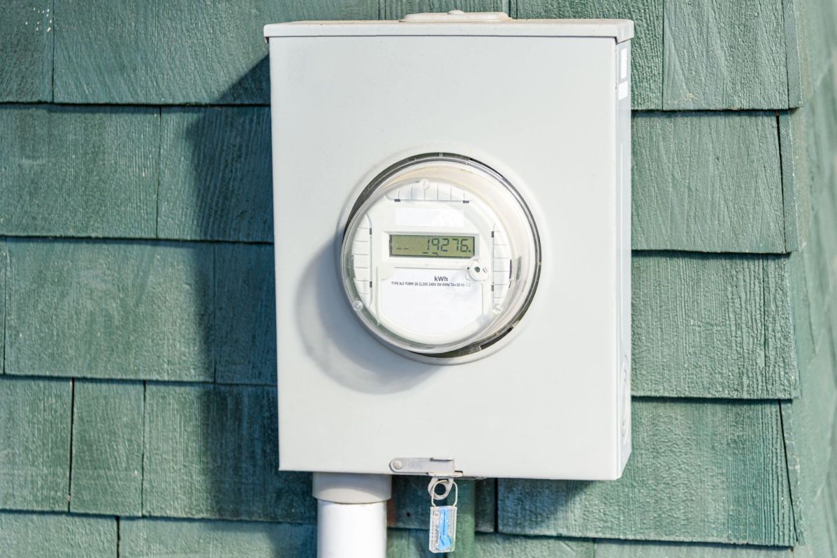 A digital meter, reading 19276, mounted on a shingle exterior wall.