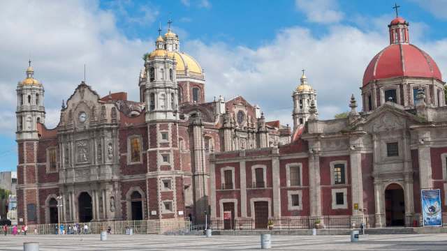 A historic church with ornate architecture, featuring golden domes and intricate stonework against a blue sky.