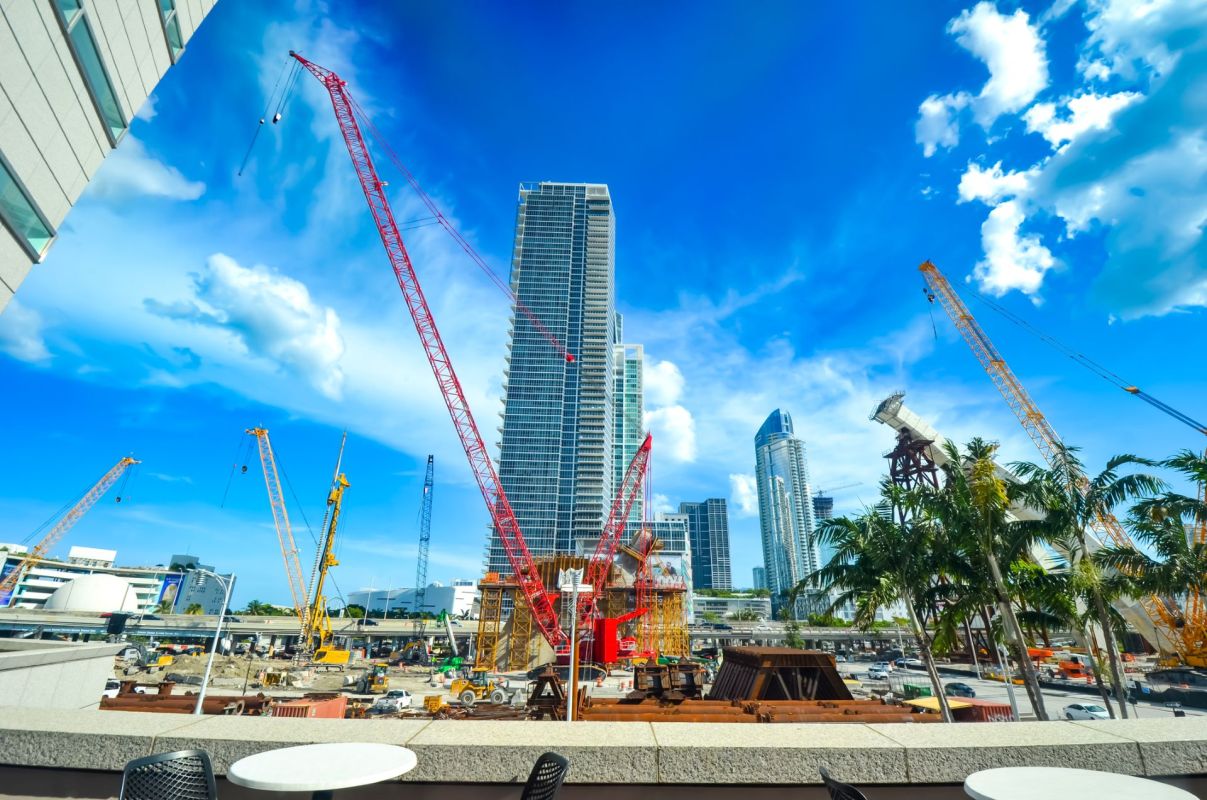 A busy construction site with cranes, skyscrapers, and clear blue skies in an urban environment.