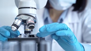 A scientist in blue gloves adjusts a microscope in a laboratory setting.
