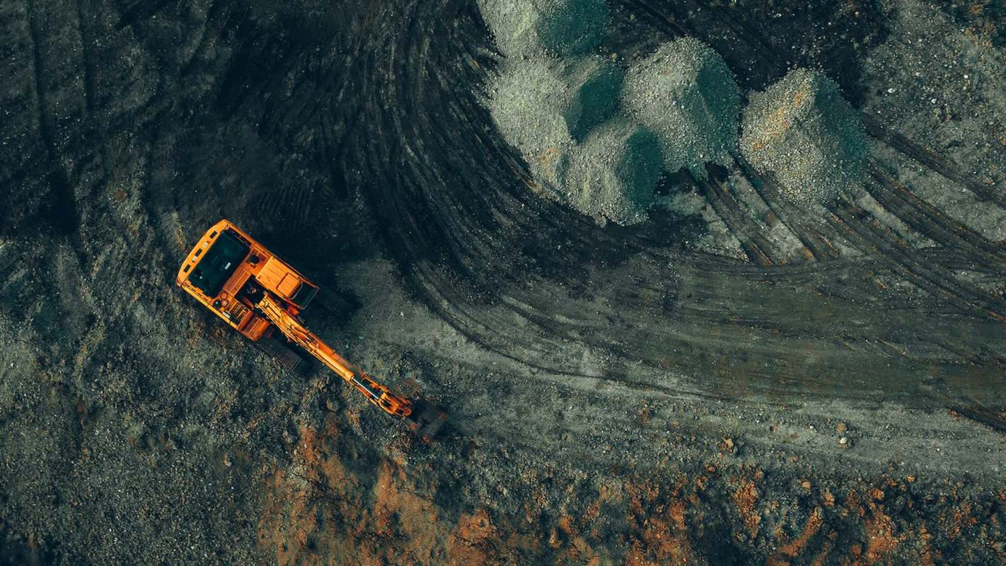 An aerial view of an orange excavator on a construction site with piles of gravel and dirt.