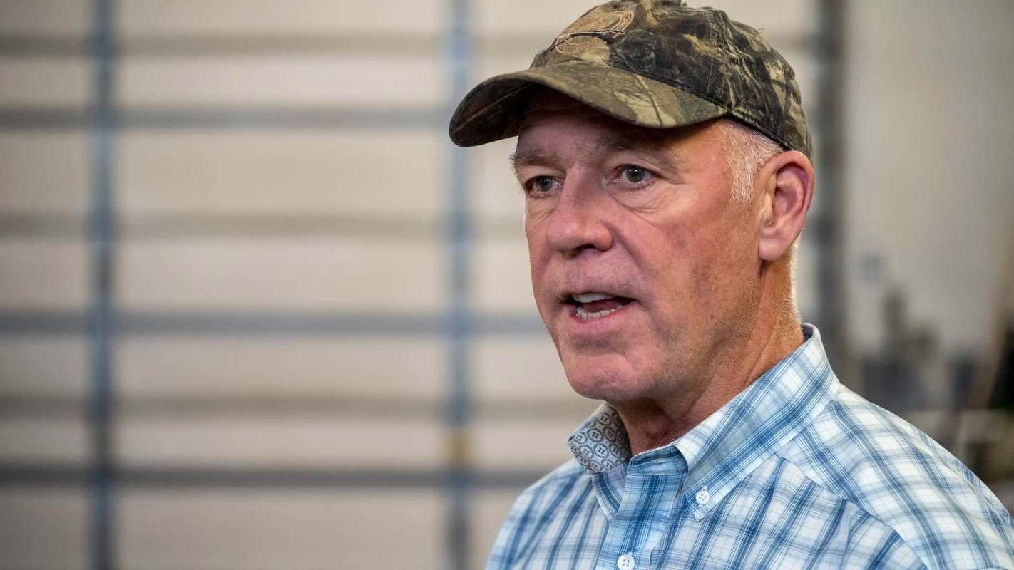 Montana governor Greg Gianforte speaking in front of a blurred industrial background.